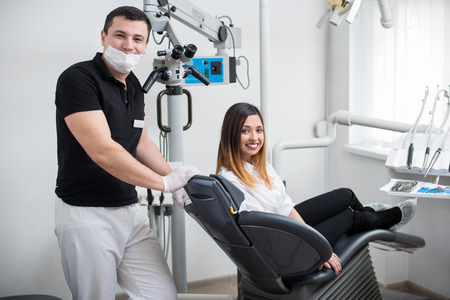 Handsome male dentist with beautiful female patient after treatment in modern dental clinic. Woman sitting in the dental chair. Dentistry. Stomatology equipmentの写真素材