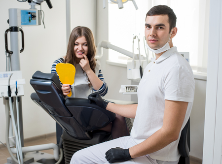 Handsome male dentist with beautiful female patient after treatment in modern dental office. Doctor looking to the camera. Dentistry. Stomatology equipmentの写真素材