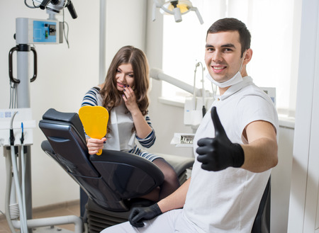 Friendly male dentist with attractive female patient after treatment in modern dental clinic. Doctor looking to the camera and showing thumbs up. Dentistry. Stomatology equipmentの写真素材