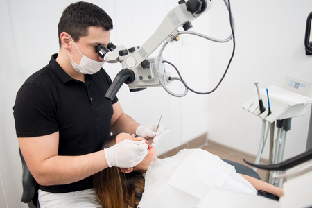 Male dentist with dental tools - microscope, mirror and probe treating patient teeth at dental clinic office. Medicine, dentistry and health care concept. Dental equipmentの写真素材