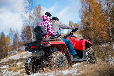 Woman sitting behind man hugging him on red four-wheeler ATV at snowy hill in the mountains . Beautiful landscape of nature in winter. Bottom viewの写真素材