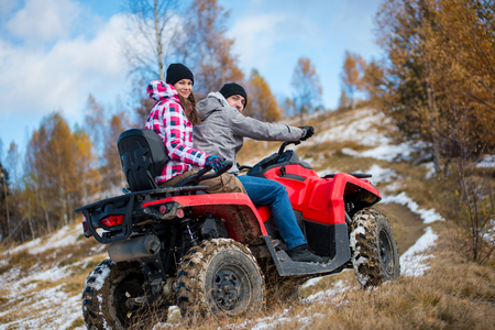 Girl sitting behind man hugging him on red four-wheeler ATV and looking to the camera at snowy hill in the mountains. Beautiful landscape of nature in winter. Bottom viewの写真素材