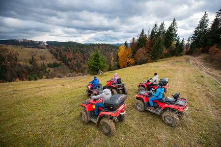 Friends driving quad bikes on the hillside at the background of autumn forest with colorful trees and mountains. Top viewの写真素材