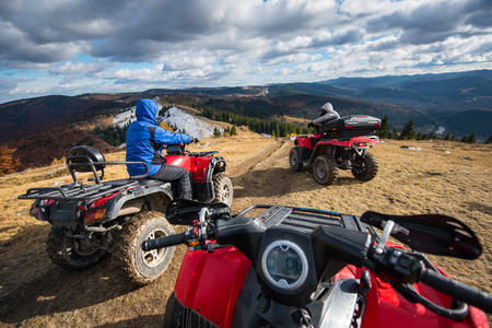 View from a quad bike with men driving an ATV in front on the top of mountain trail with perfect background mountains, forests and sky with cumulus clouds in autumnの写真素材