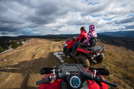 View from a quad bike. Couple driving an atv in front on the top of mountain under sky with clouds in mountainsの写真素材