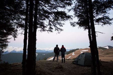 Silhouettes of two men standing near their tent on top of the mountain while out camping together nature romance travelling togetherness tourism activityの写真素材