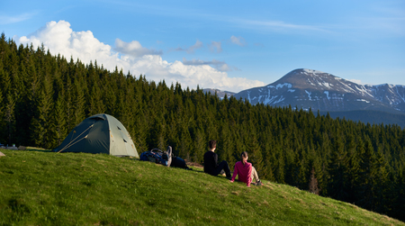 Rearview shot of two female hikers relaxing near their tent while camping outdoors in beautiful...