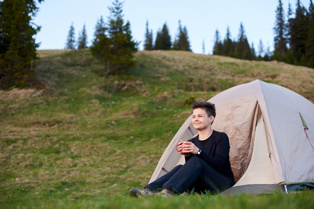 Happy female hiker drinking tea in front camp tent.の写真素材