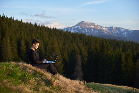 Shot of a young woman taking in the view while sitting with her laptop on top of a hill copyspace camping hiking travel tourism internet online connection mobility.の写真素材
