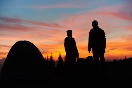 Silhouettes of a man and woman standing near their tent on top of a mountain stunning sunset on the background people lifestyle vitality sporty active travelling nature landscape sky.の写真素材