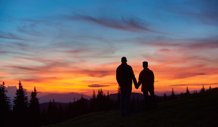 Silhouettes of a man and woman tourists standing on top of a mountain stunning sunset on the background people lifestyle vitality sporty active travelling nature landscape sky.の写真素材