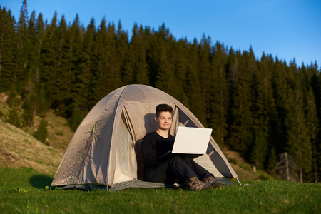 Happy young woman admiring the view while sitting in her tent in the mountains and working on a laptop copyspace technology connectivity mobility wireless connection project.の写真素材