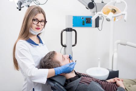 Beautiful female dentist holding dental tools - mirror and probe and getting ready for first check-up male patient in dental office. Doctor looking to the camera. Dentistry. Medical equipmentの写真素材