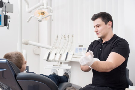 Pediatric dentist getting ready for treatment with young boy patient, wearing white gloves in dental office. Dentistry. Dental equipmentの写真素材