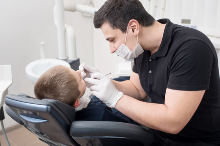 Pediatric dentist examining teeth of boy patient in dental clinic using dental tools - probe and mirror. Dentistryの写真素材