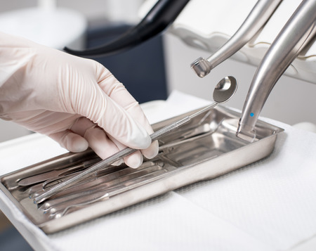 Dentist with gloved hand is picking dental tool in dental office. Close up, selective focus....