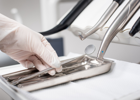 Dentist with gloved hand is picking dental mirror in dental office. Close-upの写真素材