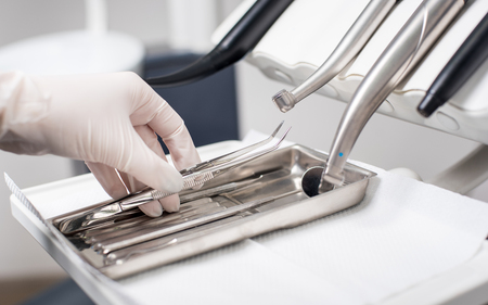 Dentist with gloved hand is picking dental tweezers in dental office. Close up, selective focus. Dentistryの写真素材