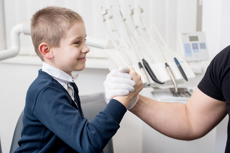 Pediatric dentist shake hands with young boy, congratulate patient for a successful operation in dental office. Dentistry. Dental equipmentの写真素材