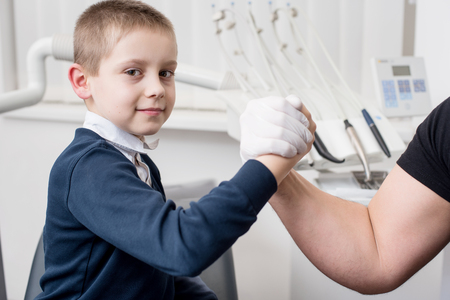 Pediatric dentist shake hands with young boy, congratulate patient for a successful treatment in dental office. Dentistry. Dental equipmentの写真素材