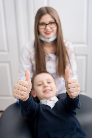 Focus of boy's hands showing thumbs up gestures of good class. Doctor and child looks at camera. Blurred backgroundの写真素材