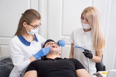 Two female dentists checking up patient teeth with dental tools - mirror and probe at dental clinic office. Medicine, dentistry and health care concept. Dental equipmentの写真素材