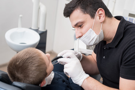 Pediatric dentist examining teeth of boy patient in dental clinic using dental tools - probe and mirror. Dentistryの写真素材