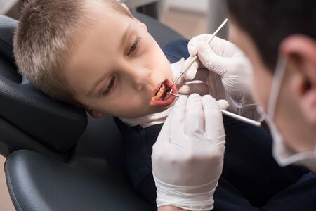 Close-up dentist examining teeth of boy patient in dental clinic using dental tools - probe and mirror. Dentistryの写真素材
