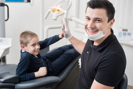 Pediatric dentist shake hands with young boy, congratulate patient for a successful operation in dental office. Dentistry. Dental equipmentの写真素材