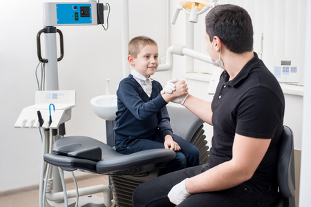 Pediatric dentist shake hands with young boy, congratulate patient for a successful treatment in dental office. Dentistry. Dental equipmentの写真素材