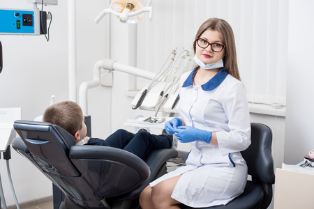 Female dentists examining and working on boy patient. Kid boy in dentist's chair. Doctor looks at camera. Dentist's officeの写真素材