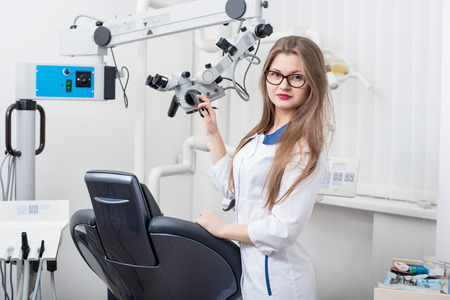 Portrait of attractive female dentist with microscope at the morden dental office. Doctor wearing glasses, white uniform and looking to the camera. Dentistryの写真素材