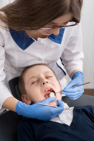 Female dentist examines the teeth of the patient child. Child mouth wide open in the dentist's chair. Close-upの写真素材