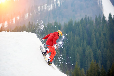 Male snowboarder in a red suit riding from the top of the snowy slope with snowboard. Skiing and snowboarding conceptの写真素材