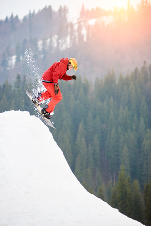 Man snowboarder jumping from the top of the snowy hill with snowboard at winter ski resort. Skiing and snowboarding conceptの写真素材