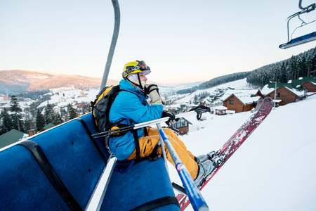Skier man sitting at ski chair lift in beautiful day looking and thoughtfully into the distance. Close-up. Concept of skiingの写真素材