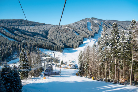 View from ski-lift at winter ski resort with an ideal landscape of snow-covered mountains, forests and ski slopes on a sunny day. Ski season and winter sports conceptの写真素材