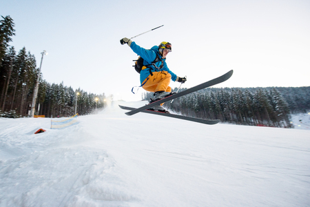 Flying skier man at jump from the slope of mountains performing a high jump and looking apprehensive about the landing with forest in background. Side viewの写真素材
