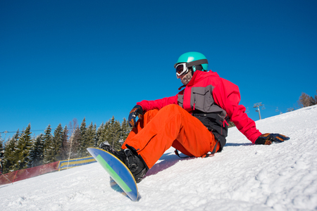 Male snowboarder sitting, relaxing on the slope of the hill at winter ski resort. Blue sky, forest on the background. copyspace lifestyle activity hobby sportsman recreation travelling Bukovelの写真素材