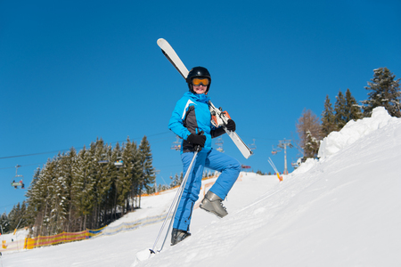 Low angle full length shot of a cheerful woman skier carrying her skis smiling to the camera while walking in the mountains copyspaceの写真素材