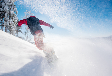 Horizontal low angle shot of a snowboarder riding the slope on a sunny winter day in the mountains. Snow in the air. copyspace freeride snowboarding active lifestyle sports recreation resortの写真素材