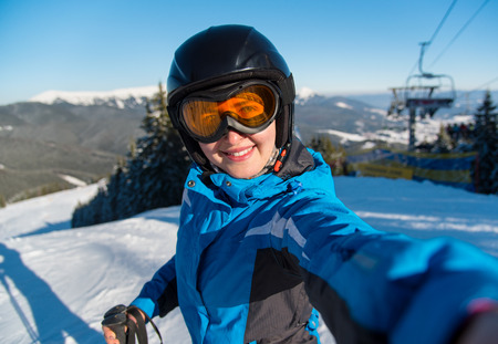 Close-up portrait of happy woman skier smiling, taking a selfie while resting on the slope after skiing in the Carpathians mountains at ski resort on a beautiful sunny winter day Bukovel, Ukraineの写真素材