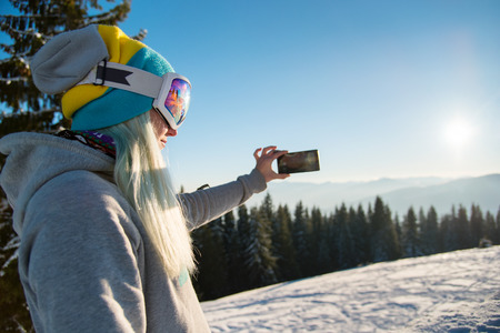 Shot of a female snowboarder using her smart phone while resting after snowboarding, taking photos of winter nature in the mountains copyspace sunset connectivity mobility lifestyle technologyの写真素材