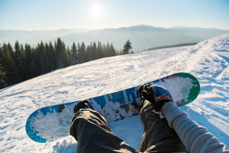 Point of view shot of a female snowboarder lying on the snow on the slope relaxing after riding, enjoying stunning view of winter mountains and sunset POV conceptの写真素材