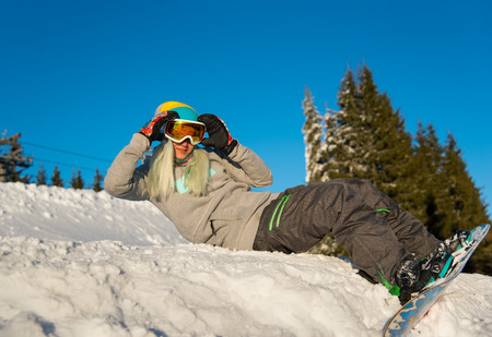 Low angle shot of a happy young woman snowboarder lying on top of the slope, relaxing outdoors on the snow on a beautiful sunny winter dayの写真素材