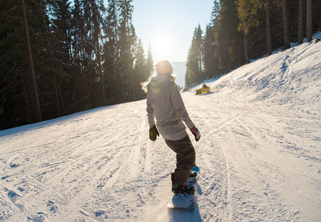 Rearview shot of a snowboarder riding the slope in the mountains on a beautiful winter sunny day sunlight flare recreation. Ski season and winter sports conceptの写真素材