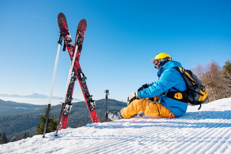 Shot of a skier sitting on slope near his skiing equipment relaxing enjoying beautiful snowy mountains view people living enjoyment recreation travelling riding winter resortの写真素材