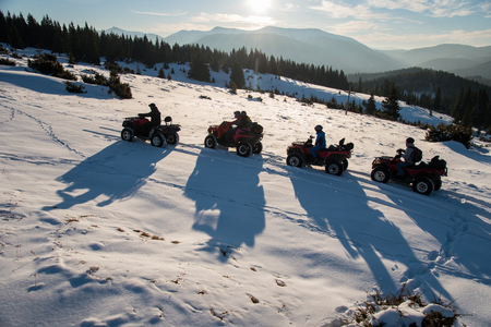 Group of people enjoying sunset, sitting on off-road four-wheelers ATV bikes on snow in the the mountains in winterの写真素材