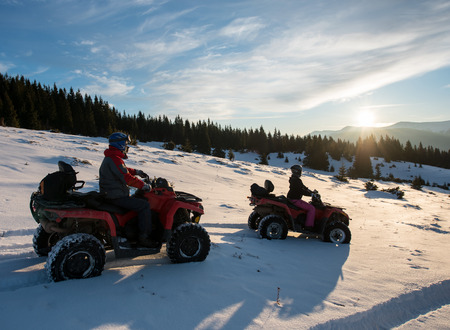 Man and woman sitting on four-wheelers ATV bikes on snow, enjoying sunset in the the mountains in winterの写真素材