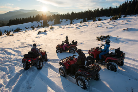 Group of people sitting on off-road quad bikes, enjoying beautiful sunset in the the mountains in winterの写真素材